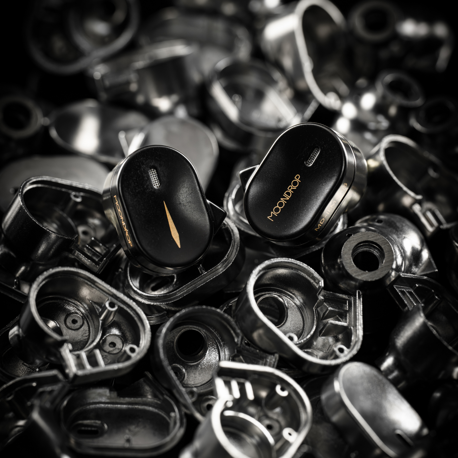 Moondrop CHU III earphones in black with gold accents, shown among metal components on a dark background.